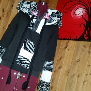 May include: Black hooded sweatshirt with white and black zebra print fabric patches on the sleeves and body. The hoodie has a black zipper and black drawstrings.