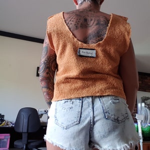 May include: A woman wearing a light orange, terry cloth top with a white label that says "Von Trapp" and light blue denim shorts with a distressed look.