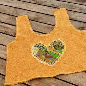 May include: A yellow crocheted tank top with a heart-shaped patch made of colorful fabric.