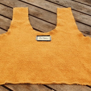 May include: A mustard yellow sleeveless top made of a soft, fuzzy fabric. The top has a scoop neck and a raw edge hem. A small white tag with the text "Blue Vanilla" is attached to the front of the top.
