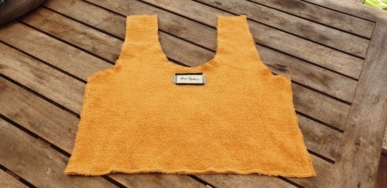 May include: A mustard yellow sleeveless top made of a soft, fuzzy fabric. The top has a scoop neck and a raw edge hem. A small white tag with the text "Blue Vanilla" is attached to the front of the top.