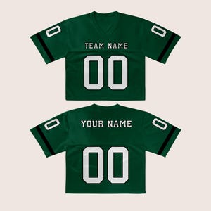 Puede incluir: Dos camisetas de f&uacute;tbol verdes con n&uacute;meros y letras blancas. La camiseta delantera dice "TEAM NAME" encima del n&uacute;mero "00". La camiseta trasera dice "YOUR NAME" encima del n&uacute;mero "00". Cada camiseta tiene una franja negra en las mangas.