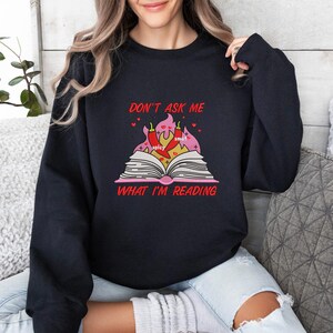 May include: Black sweatshirt with the text "DON'T ASK ME WHAT I'M READING" in red. The graphic features an open book with flames, chili peppers, and the words "spicy" and "smut".