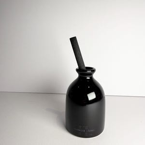 May include: A black ceramic essential oil diffuser bottle with a dark grey reed stick. The bottle has a rounded base and a narrow neck. The text "TRANQUIL LIVING" is printed on the front of the bottle.