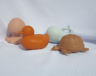 Puede incluir: Colección de cuatro juguetes de baño en colores pastel: un pulpo melocotón, un pato naranja, una ballena azul claro y una tortuga marrón. Los juguetes están hechos de un material suave.