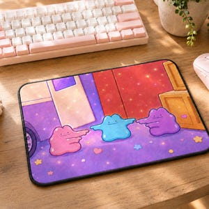 May include: A rectangular mouse pad featuring a vibrant illustration of three blob-like creatures in pink, blue, and purple. The characters are pointing at each other against a purple background with small colorful stars and hearts scattered throughout.