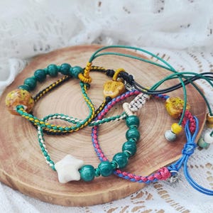 May include: A collection of handmade bracelets with various designs and colors. The bracelets feature beads in shades of green, yellow, and white, along with star-shaped and round charms. They are displayed on a wooden surface.