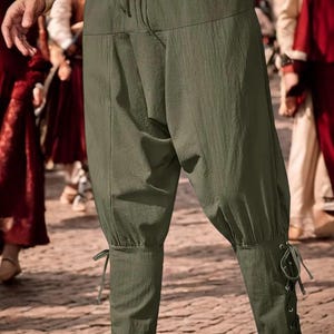 May include: Olive green medieval-style trousers with a drawstring waist and lace-up details at the ankles. The loose-fitting trousers are made of a textured fabric, suitable for historical reenactments or themed events.