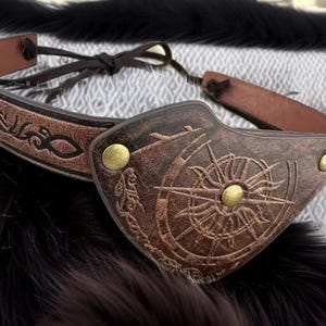 May include: A brown leather mask featuring a compass rose design and brass studs. The mask has a dark brown leather strap, suitable for costume or cosplay purposes.