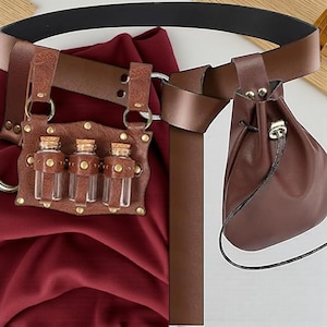 Może przedstawiać: Brązowy skórzany pasek z sakiewką i uchwytem na trzy małe szklane butelki z korkami. Pasek ma czarny pasek i jest umieszczony na bordowym tle z tkaniny.