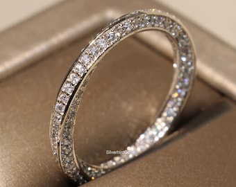 May include: A silver ring with a double band design, encrusted with numerous small, clear gemstones. The ring is set against a neutral background, highlighting its sparkle and intricate details. The ring appears to be a piece of fine jewelry.