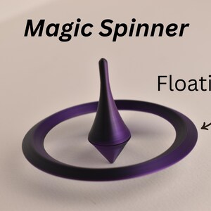 Może przedstawiać: Fioletowa zabawka Magic Spinner z centralnym stożkowym wrzecionem i oddzielnym otaczającym pierścieniem. Tekst Magic Spinner znajduje się u góry, a słowo Floating ze strzałką wskazującą na pierścień jest widoczne po prawej stronie.