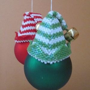 May include: Two Christmas baubles with knitted hats. One bauble is red with a white and red striped hat. The other bauble is green with a white and green striped hat.