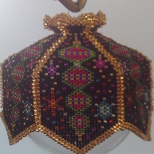 May include: A beaded Christmas ornament with a gold trim and a geometric pattern in shades of black, red, green, and gold.