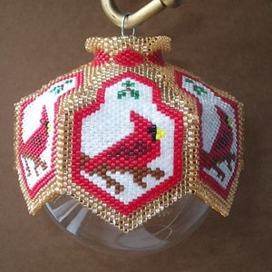 May include: A beaded Christmas ornament with a red cardinal design. The ornament is made of small beads in gold, white, red, and green colors. The ornament is hanging from a gold hook.