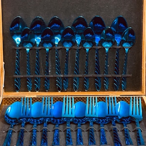 Könnte beinhalten: Ein komplettes Set aus blauen Edelstahlbesteck, einschließlich Löffeln und Gabeln, ordentlich in einer Holzaufbewahrungsbox angeordnet. Das Besteck hat eine glänzende Oberfläche und ein gedrehtes Griffdesign, perfekt für ein formelles Esszimmer.