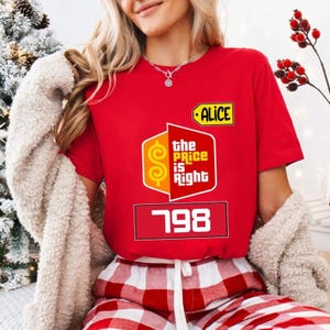 May include: A red t-shirt with the "The Price Is Right" logo, the name "ALICE", and the number "798". The person is wearing red and white checked pyjama bottoms. The shirt is a vibrant red colour.