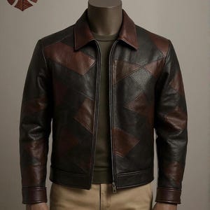 Puede incluir: Chaqueta de cuero negra y marrón con diseño geométrico. La chaqueta tiene cuello, cierre de cremallera y puños marrones. El logotipo de la marca "LEATHEXOTIQUE" es visible en la esquina superior izquierda.
