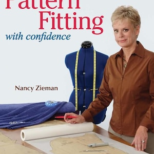 May include: A book cover with the title "Pattern Fitting" in red letters, with the subtitle "with confidence." A woman in a brown shirt stands next to a blue dress form. Sewing patterns and tools are on the table.