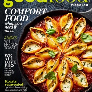 Puede incluir: La portada de la revista BBC Good Food presenta conchas de pasta rellenas de queso y hierbas, dispuestas en un patr&oacute;n circular en una sart&eacute;n de hierro fundido, con una base de salsa de tomate. Tambi&eacute;n se ven el t&iacute;tulo y el contenido de la revista.