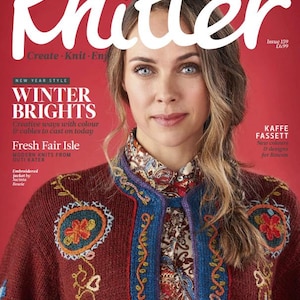 以下が含まれることがあります： 女性がボルドー色の刺繍入りジャケットを着ているThe Knitter誌の表紙。表紙には、冬のニットプロジェクトや新しいデザインに関するテキストが含まれています。雑誌の背景は赤色です。