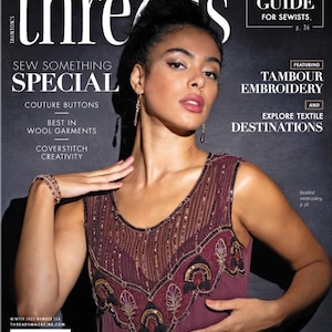 Può includere: La copertina della rivista Threads presenta una donna con un abito bordeaux con perline. Il titolo della rivista è in grandi lettere bianche. Il testo include "Sew Something Special" e "Gift Guide for Sewists".
