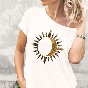 White organic cotton T-shirt with gold sun and moon celestial design worn by a woman outdoors. Minimalist astrology graphic.