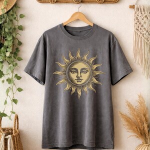 Charcoal gray celestial sun face t-shirt hanging on a wooden hanger, showing a vintage boho astrology design in a clean product display