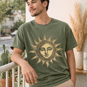 Man wearing an olive green / moss celestial graphic tee with vintage sun design, styled as a unisex boho astrology shirt for relaxed everyday wear