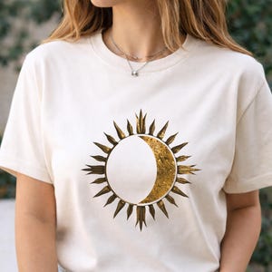 White organic cotton T-shirt with gold sun and moon cosmic design worn by a man outdoors. Minimalist astrology graphic.