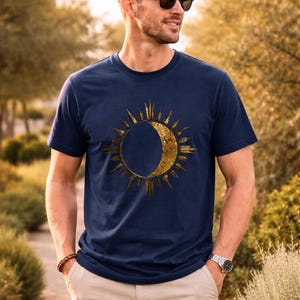 Navy blue organic cotton T-shirt with gold sun and moon cosmic design worn by a man outdoors. Minimalist astrology graphic.