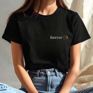Woman wearing an black t-shirt with small "forever" sun and moon chest print. Celestial boho design, gift for her and him.