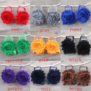 K&ouml;nnte beinhalten: Set mit 10 Paaren Babysandalen mit Blumenverzierungen in verschiedenen Farben, darunter Rot, Grau, K&ouml;nigsblau, Smaragdgr&uuml;n, Gold, Schwarz, Lila, Marineblau und Braun.