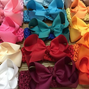 May include: A collection of colourful hair bows with crocheted headbands. The bows are arranged in a rainbow pattern, starting with pink and ending with orange.