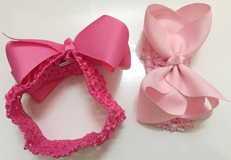 May include: Two pink hair bows with a crocheted headband. One bow is a simple bow and the other is a headband with a bow.
