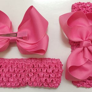 May include: Two pink hair bows, one with a clip and one attached to a pink elastic headband. Both bows are made of a shiny, satin-like material.