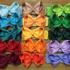 May include: Twenty-four hair bows in a variety of colours, including pink, blue, green, yellow, orange, red, purple, brown, black, and white. Each bow is attached to a crocheted headband.