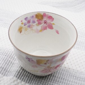 Pu&ograve; includere: Una ciotola in ceramica bianca con un motivo floreale rosa, viola e oro. I fiori sono dipinti all'esterno della ciotola. La ciotola ha una superficie leggermente strutturata e un bordo marrone.