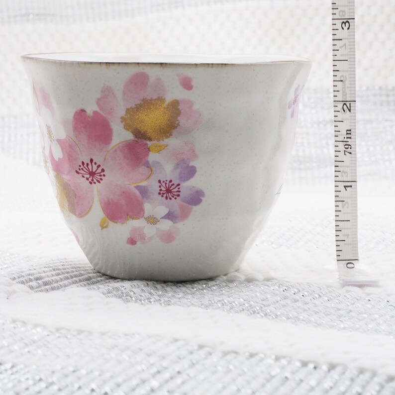 Pu&ograve; includere: Una tazza da t&egrave; in ceramica bianca con un motivo floreale con fiori rosa, viola e oro. La tazza &egrave; alta circa 7,6 cm. La tazza ha una superficie strutturata e una forma leggermente irregolare.