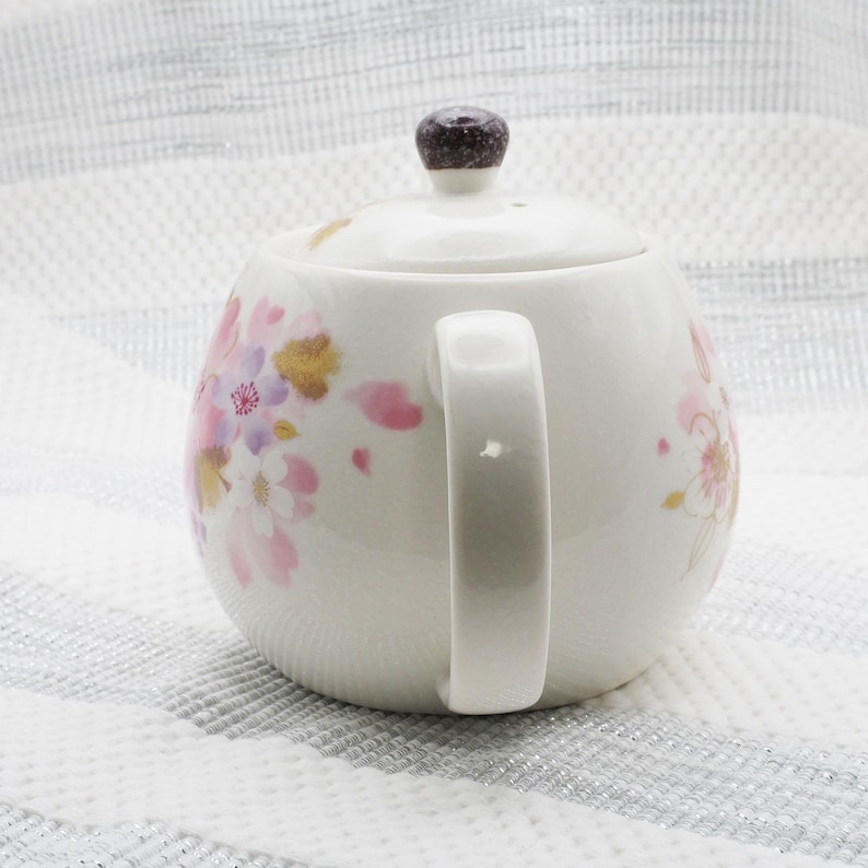 Pu&ograve; includere: Teiera in ceramica bianca con coperchio e manico. La teiera &egrave; decorata con motivi floreali rosa, oro e viola. Il coperchio ha un pomello marrone scuro. La teiera &egrave; progettata per preparare il t&egrave;.