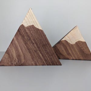 Peut inclure: Deux sculptures de montagnes en bois. Les formes triangulaires sont en bois clair avec une teinture marron foncé sur la partie inférieure, ressemblant à une chaîne de montagnes. Les sommets ne sont pas teints.