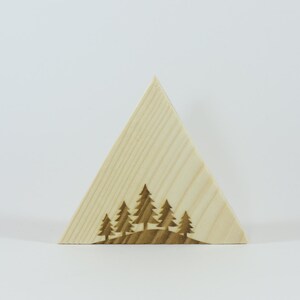 Peut inclure: Un élément décoratif en bois de forme triangulaire. Le bois de couleur claire présente un motif gravé au laser d'une petite forêt de pins sur une colline. La pièce mesure environ 15 cm de haut.