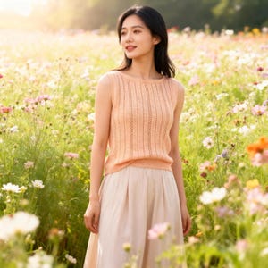 May include: A sleeveless peach-colored knit top with vertical ribbed detailing. The top is paired with a light beige skirt. The image is set in a field of colorful wildflowers, bathed in sunlight.