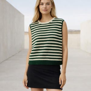 May include: A sleeveless sweater vest with horizontal stripes in dark green and cream. The vest is paired with a black mini skirt. The model is standing in a neutral-toned outdoor setting.