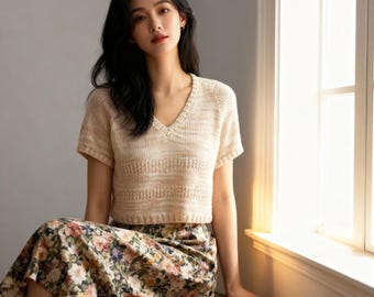 Puede incluir: Top de punto beige con cuello en V y mangas cortas. La parte superior tiene un diseño horizontal en el pecho. La modelo lleva una falda con estampado floral. El atuendo es adecuado para ropa casual.