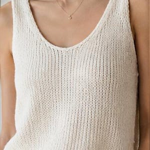 Peut inclure: Un débardeur en tricot couleur crème sans manches avec une texture côtelée et une encolure dégagée, associé à un pantalon blanc doté d'un seul bouton visible à la taille. Le haut a une coupe ample et un ourlet fini, créant un ensemble neutre.
