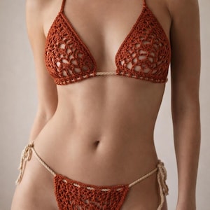 May include: A rust-colored crochet bikini set. The triangle top and thong-style bottoms feature a delicate openwork design with cream-colored string ties. The bikini is made of a soft, textured yarn.