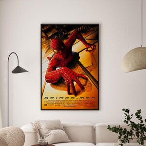 May include: Framed movie poster for the film Spider-Man. The poster features the superhero in a red and black suit, with a webbed design, in a dynamic pose against a yellow and orange background. The title "SPIDER-MAN" is prominently displayed.