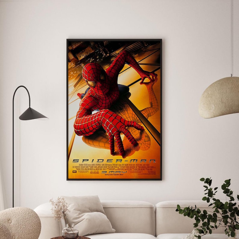 May include: Framed movie poster for the film Spider-Man. The poster features the superhero in a red and black suit, with a webbed design, in a dynamic pose against a yellow and orange background. The title "SPIDER-MAN" is prominently displayed.