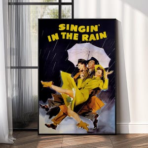 Puede incluir: Póster enmarcado con el título "Singin' in the Rain". La obra de arte representa a tres personas bailando bajo la lluvia, una de ellas sosteniendo un paraguas. Los bailarines visten trajes amarillos y marrones sobre un fondo oscuro.